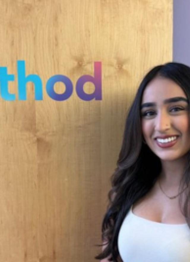 Simrun Bhandal standing in front of a wooden wall with the logo 'method' in colorful text.