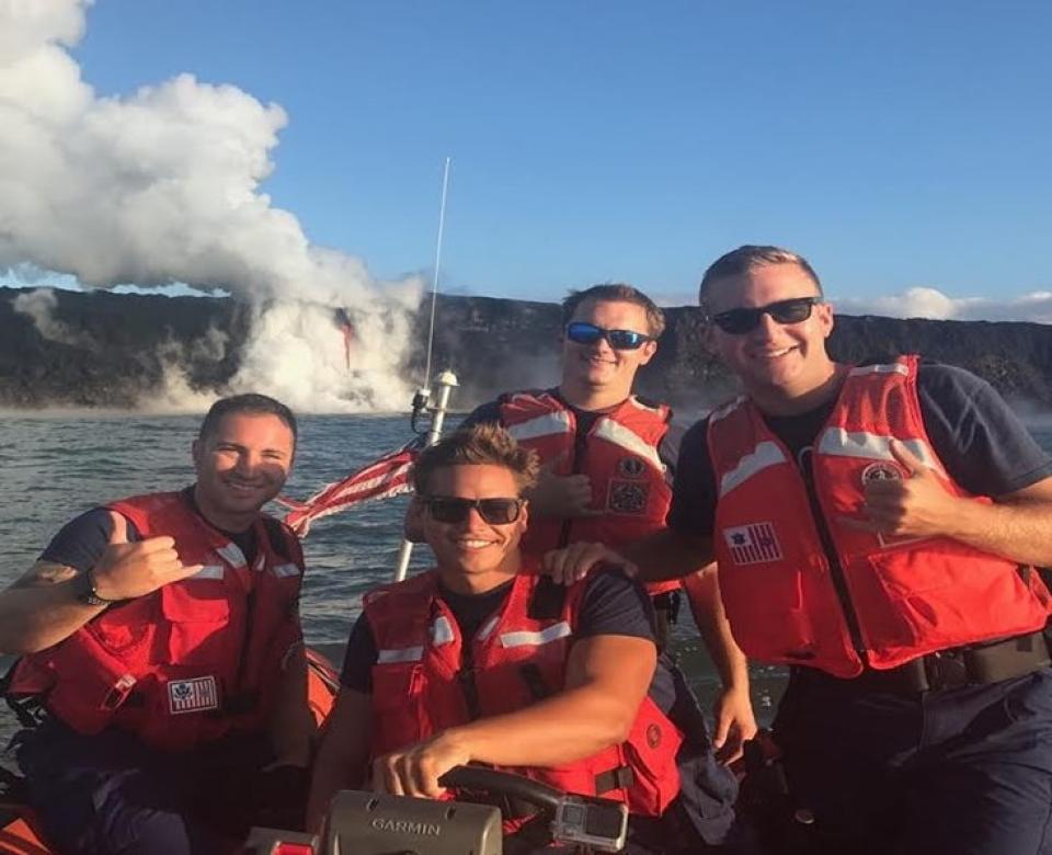 Four members of the U.S. Coast Guard are aboard a small boat in the ocean, all wearing red life vests